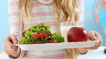 close up of girl holding school cafeteria tray with milk apple and sandwich