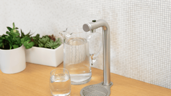 Marco beverage dispenser on light wood counter, with pitcher and glass filled with water