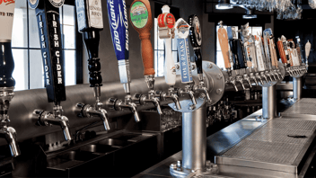 Row of Perlick beer taps behind a bar. Each tap has a different handle for each individual brand of beer. 