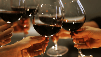 Four hands holding wine glasses with red wine to each other