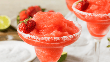 Two strawberry margaritas with salt on rims. Lime slice and plate of salt in background.