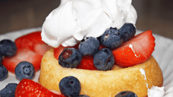 Sponge cake with blueberries and strawberries on top. Whipped cream on top of cake and berries.