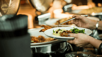 Hand holds a white plate and adding food from chafing dishes on a buffett