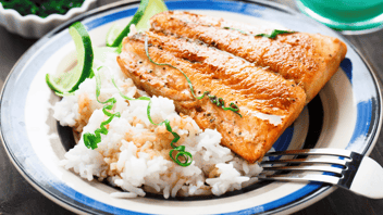 Blue white plate holds a piece of steamed salmon and rice. Two slices of twisted lime are also on the plate and a fork is on the side.