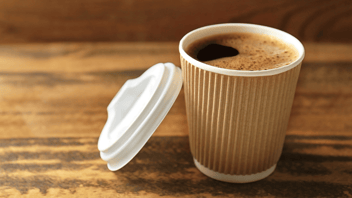 To-go cup of hot drink on a wooden surface with white lid leaning against it