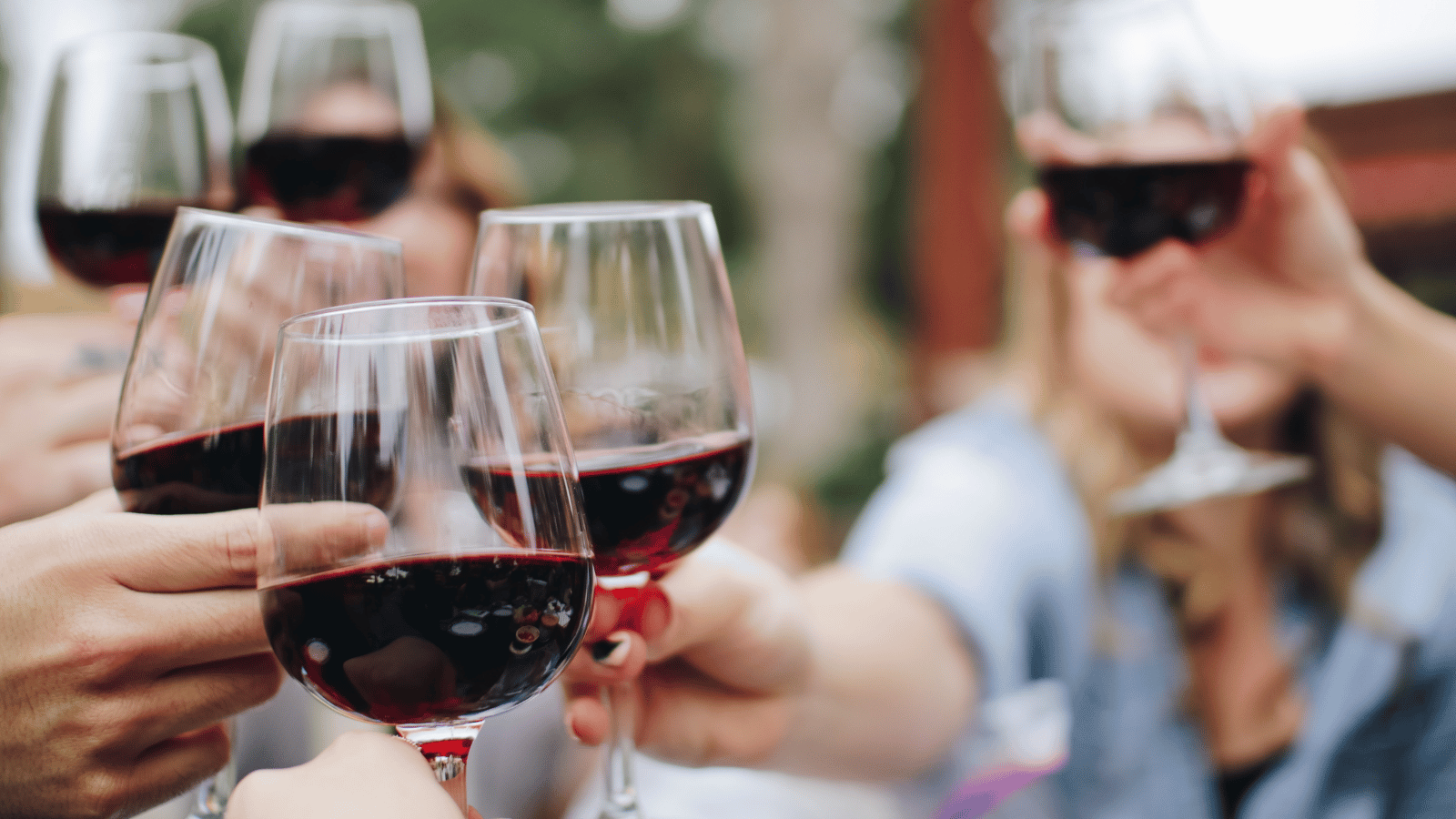 Three hands holding glasses of red wine together cheering with three separate hands holding glasses of red wine in background