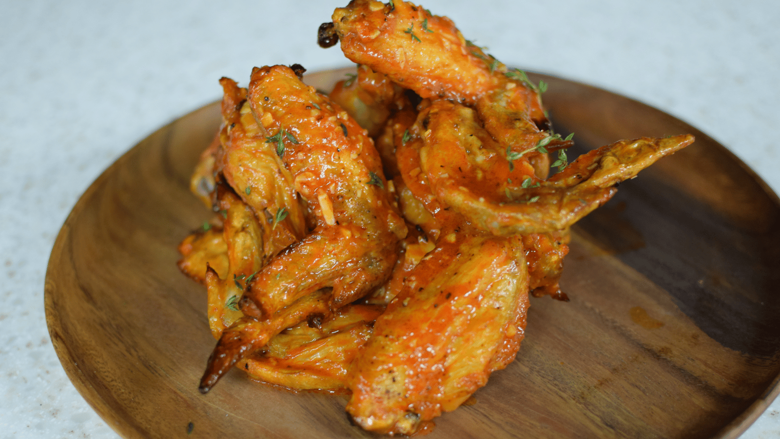 Pile of crispy chicken wings on top of wood plate on white countertop
